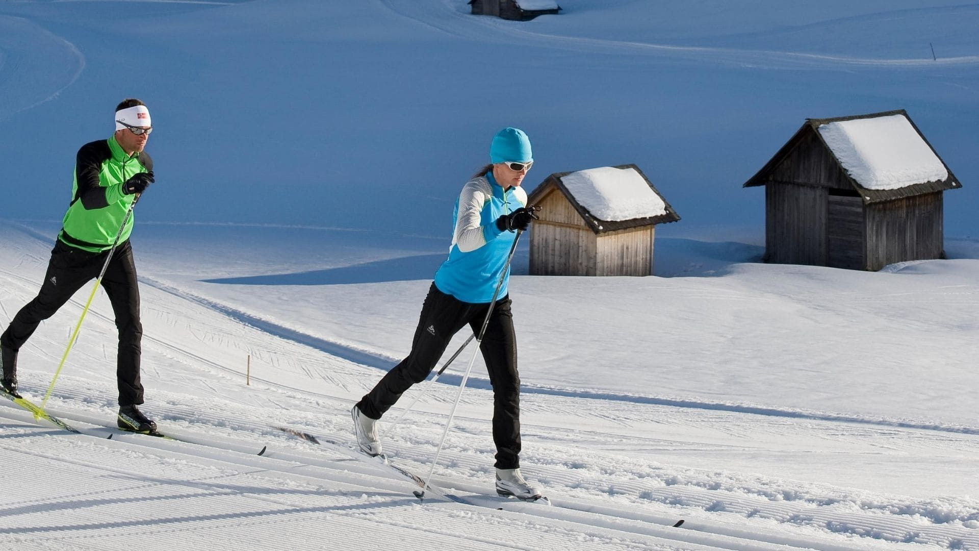 Skieurs de fond sur piste damée près de granges en bois - Alpes