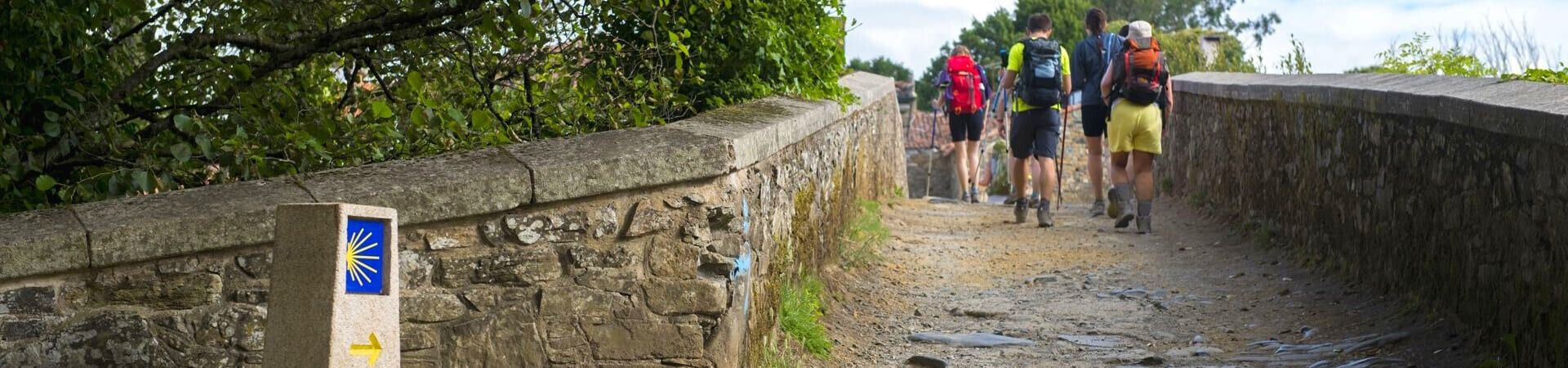 Pèlerins sur un pont de pierre avec balise coquille Saint-Jacques - Camino de Santiago - Espagne